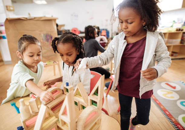 девушки играют с деревянными блоками, создавая новое здание - preschooler toddler classroom learning стоковые фото и изображения