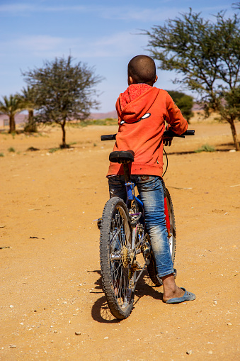 Tinzouline, Morocco - February 26, 2016: Rear view of Moroccan boy riding bicycle in desert in Tinzouline village in Morocco