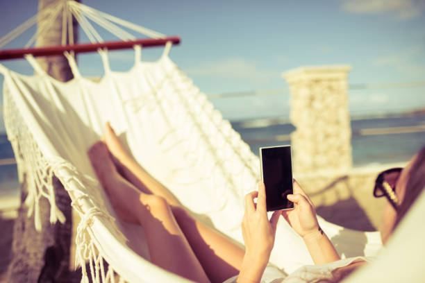 istock Woman using surfing the net while relaxing in a hammock by the beach 893659480