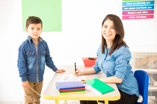 simpatico insegnante in età prescolare che classifica il lavoro dello studente - grading teacher desk writing foto e immagini stock