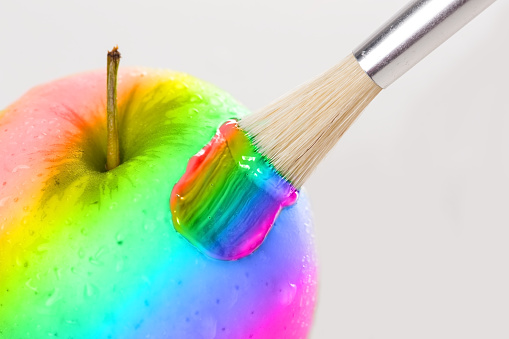 Rainbow apple close-up with water drops being painted on white background