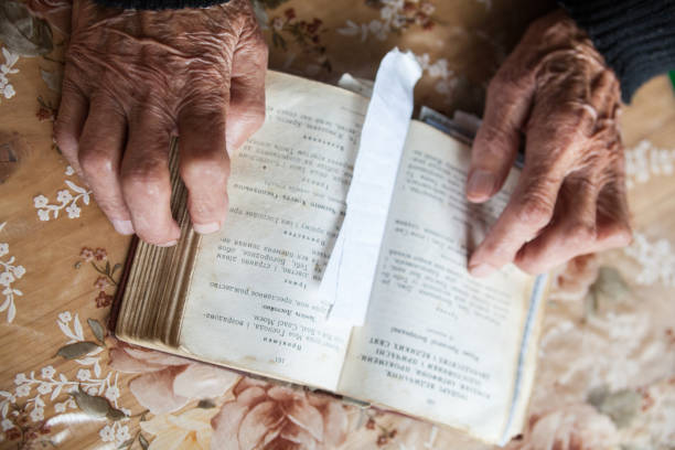 istock Old woman hands on the open prayer book. 893716270