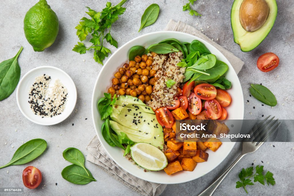 healhty vegan lunch bowl. Avocado, quinoa, sweet potato, tomato, spinach and chickpeas vegetables salad healhty vegan lunch bowl with ingredients. Avocado, quinoa, sweet potato, tomato, spinach and chickpeas vegetables salad. Top view Vegan Food Stock Photo