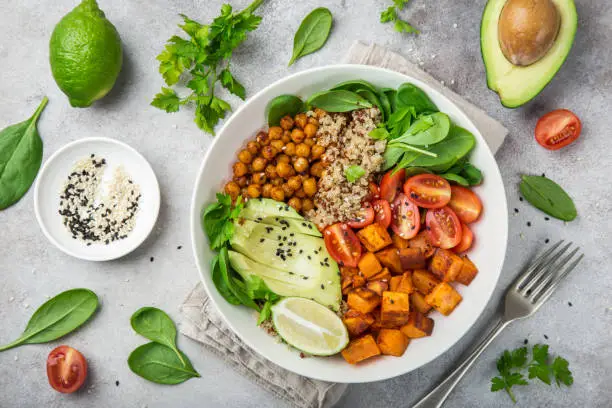 Photo of healhty vegan lunch bowl. Avocado, quinoa, sweet potato, tomato, spinach and chickpeas vegetables salad