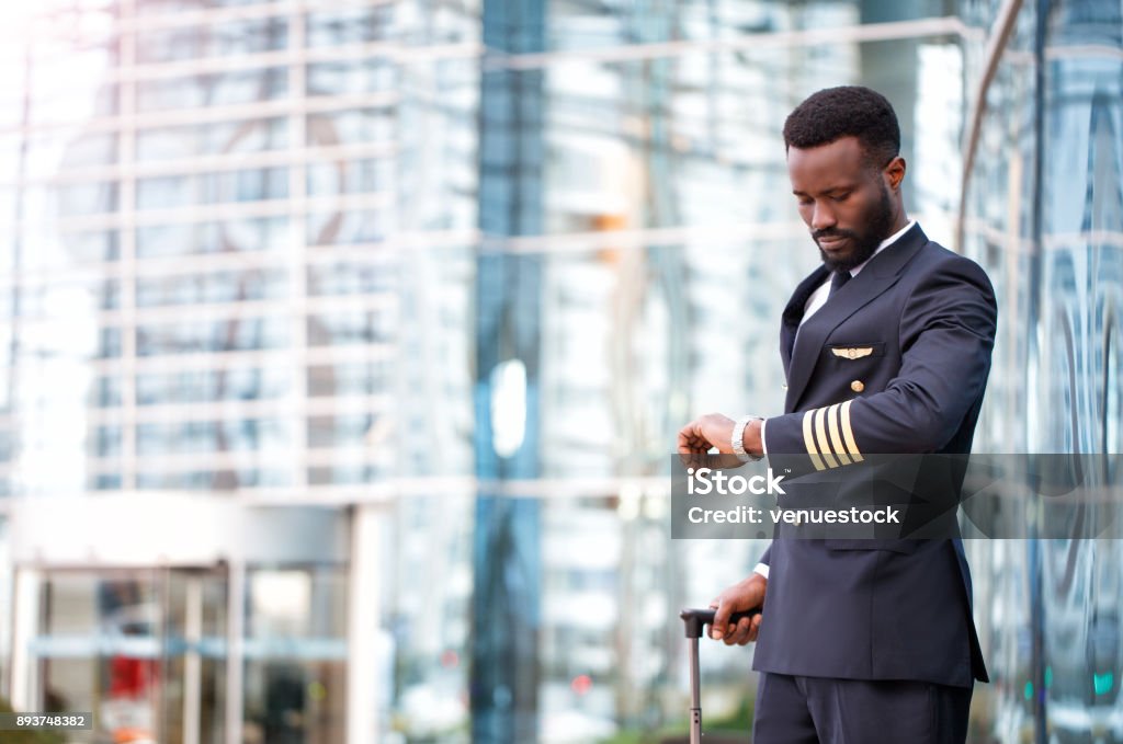 Pilot waiting the flight Afro American Pilot, Airport, Looking, Watch, Uniform, Luggage Pilot Stock Photo