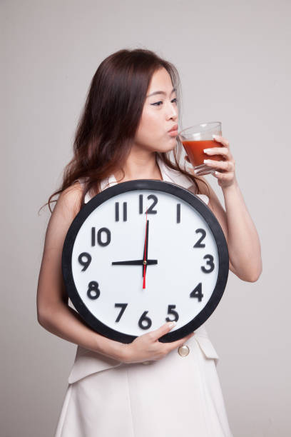 istock Young Asian woman with tomato juice and clock. 893789936