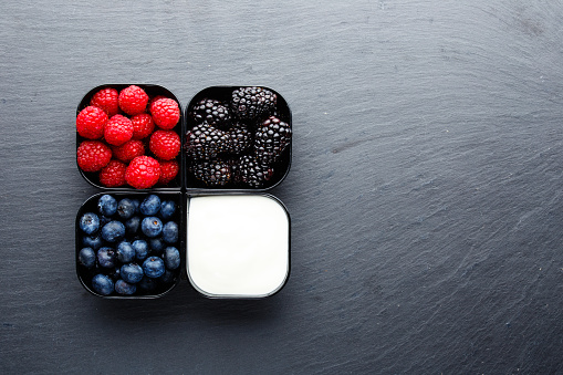 Small cups full of berries with Greek yogurt on dark stone surface