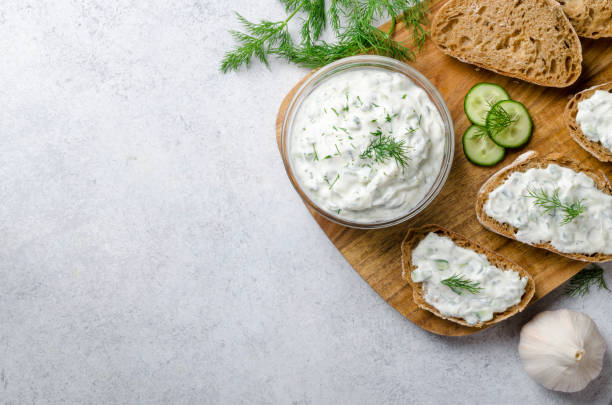 Homemade greek tzatziki sauce in a glass bowl with ingredients and sliced bread on a wooden board and light stone background. Cucumber, lemon, dill. Top view, horizontal image, copy space Homemade greek tzatziki sauce in a glass bowl with ingredients and sliced bread on a wooden board and light stone background. Cucumber, lemon, dill. Top view, horizontal image, copy space tzatziki stock pictures, royalty-free photos & images