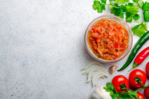 Traditional mexican homemade salsa sauce with ingredients, tomatoes, pepper, onion, cilantro on a light stone table. Top view, horizontal image, copy space