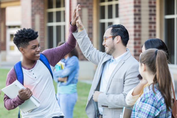 High school teacher gives student a high five Friendly Hispanic high school teacher gives a male student a high five before school starts. They are standing outside the school. teenager back to school group of people student stock pictures, royalty-free photos & images