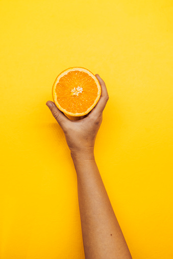 Photo of Unrecognizable Caucasian Female hand  holding fresh Orange - Fruit on a yellow  background. Home grown Orange, organic food that the girl holds in her hand. Woman holding yellow Raw Food fruit.