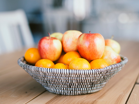 A woven fruit basket sitting on a wood table inside a home.