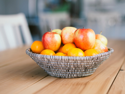 A woven fruit basket sitting on a wood table inside a home.