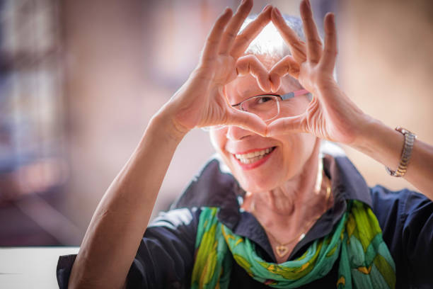 Senior woman sending love Cute senior old woman making a heart shape with her hands and fingers senior women stock pictures, royalty-free photos & images