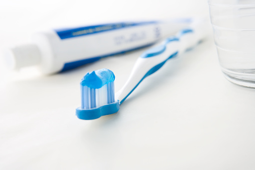 Toothpaste on toothbrush, with glass of water and paste tube