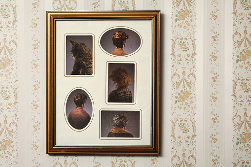 A picture frame hangs on a wall with an ornate frame and retro style, the people posing in the portrait facing the wrong direction, only the back of their heads and bodies visible.  Horizontal with copy space.