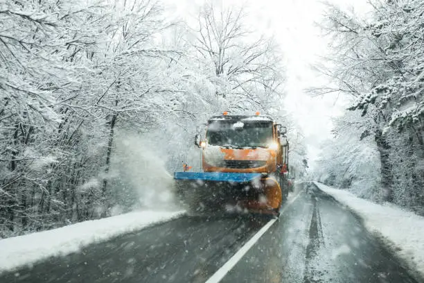 Front view of snowplow service truck and  gritter spreading salt on the road surface to prevent icing in stormy snow winter day.