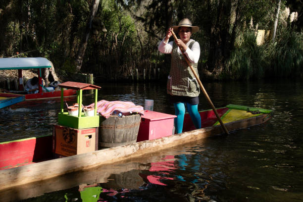 woman on trajinera Xochimilco, Mexico City, Mexico - 2017: A woman in a trajinera (a local type of boat) sells cold beverages to people in other trajineras on a city canal trajinera stock pictures, royalty-free photos & images