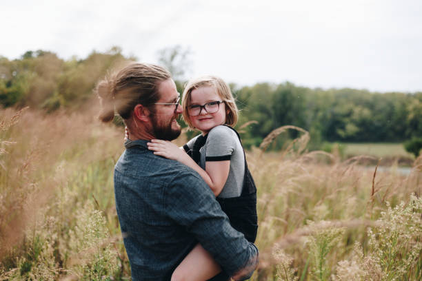 A caring dad hugs his daughter in a sunlit field, capturing a tender family moment filled with warmth, affection, and togetherness.