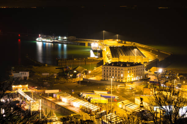 The Cruise Terminal and Inner Harbour at The Port of Dover in Kent, UK, photographed from the cliffs at Dover. The Port of Dover is Europe’s busiest ferry port and an international gateway for the movement of passengers and trade. It is also the second busiest cruise port in the UK. The port includes a cargo terminal, a marina and several other business. The largest of the terminals, Cruise Terminal 2 (seen here at night) was purpose built in 2000 along the lines of an airport terminal. Lights from Calais in France can be seen in the background across the English Channel.