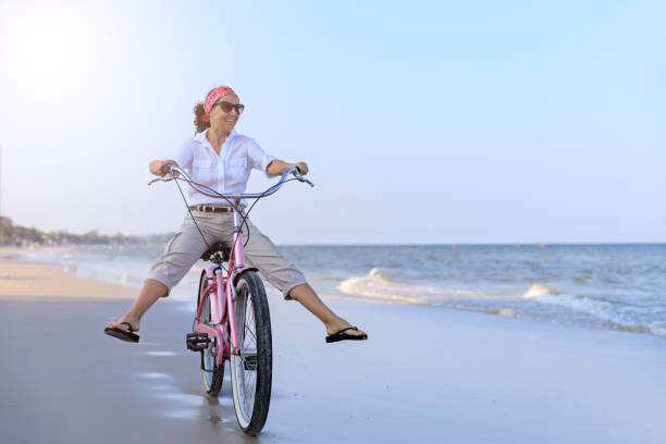 幸せな女のビーチで自転車に乗る - mature adult vacations action adult ストックフォトと画像