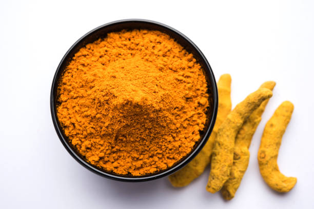 istock Turmeric powder in ceramic bowl with raw dried turmeric over plain background 894159742