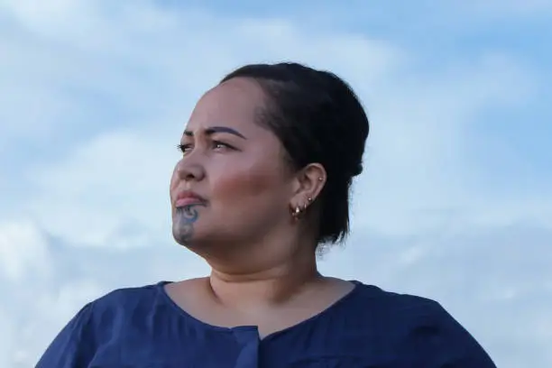 A Maori lady with a moko (traditional new zealand facial tattoo) with a blue cloudy sky behind her