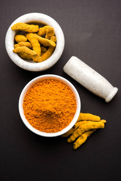 istock Turmeric powder in ceramic bowl with raw dried turmeric over plain background 894162866