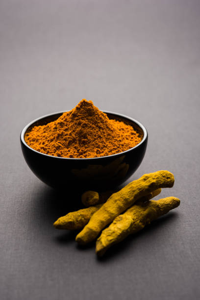 istock Turmeric powder in ceramic bowl with raw dried turmeric over plain background 894172672