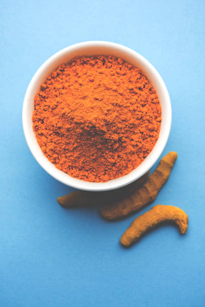 istock Turmeric powder in ceramic bowl with raw dried turmeric over plain background 894181590