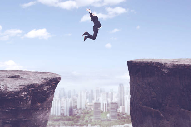istock Happy businessman jumping through gap cliff 894184114