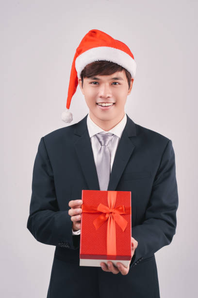 istock Smiling asian businessman in santa hat presenting gift isolated on white 894184246
