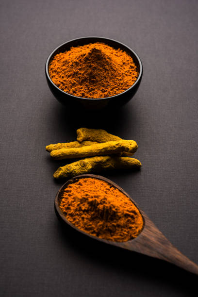 istock Turmeric powder in ceramic bowl with raw dried turmeric over plain background 894186834