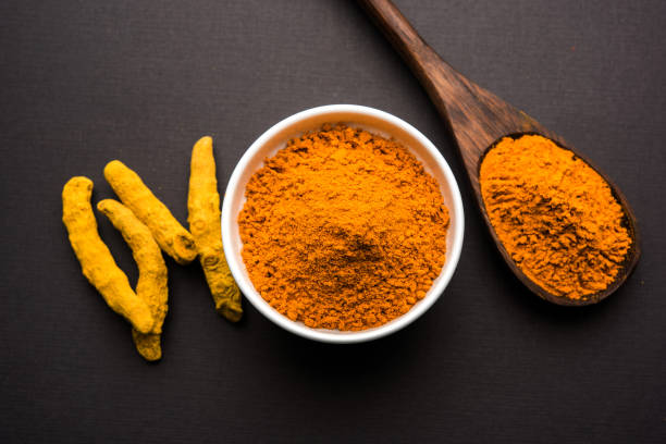 istock Turmeric powder in ceramic bowl with raw dried turmeric over plain background 894194220