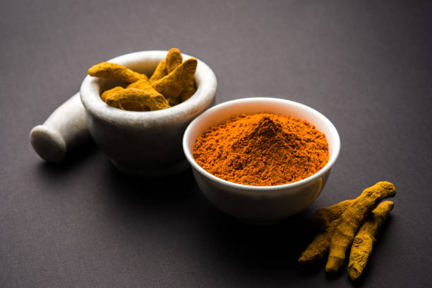 istock Turmeric powder in ceramic bowl with raw dried turmeric over plain background 894194542