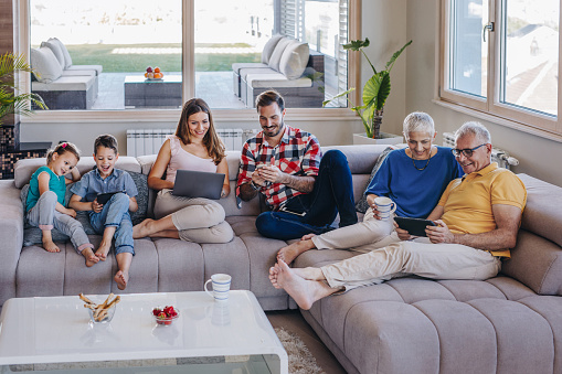 Smiling multi-generation family using wireless technology while relaxing in the living room.