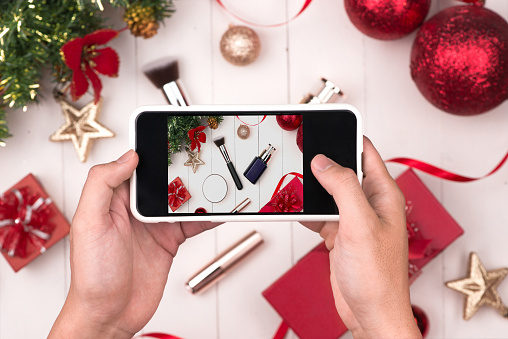 Hands holding mobile taking photo of christmas make up cosmetics products