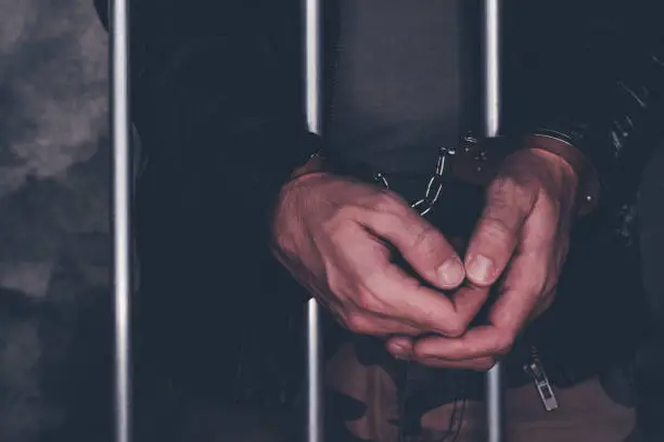 Photo of Handcuffed man behind prison bars