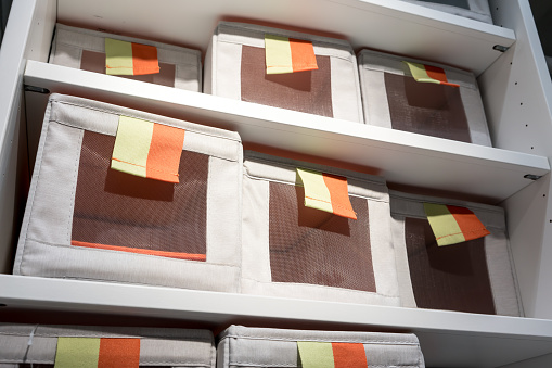 Fabric storage boxes in square shape with orange and yellow pull to open tag arranged on white shelf. Idea for home organizer.