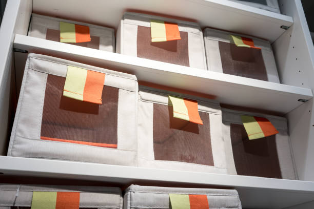 Fabric storage boxes in square shape with orange and yellow pull to open tag arranged on white shelf. Idea for home organizer. stock photo
