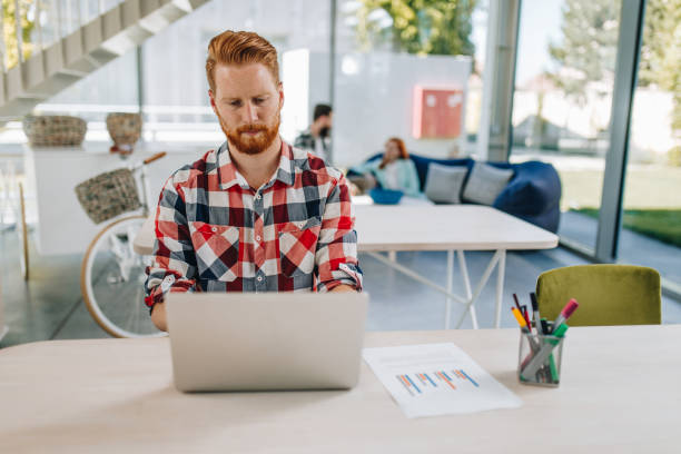 istock Serious redhead freelancer working on laptop at casual office. 894299262