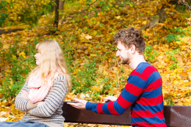 istock Two people sit on bench in park arguing. 894322582