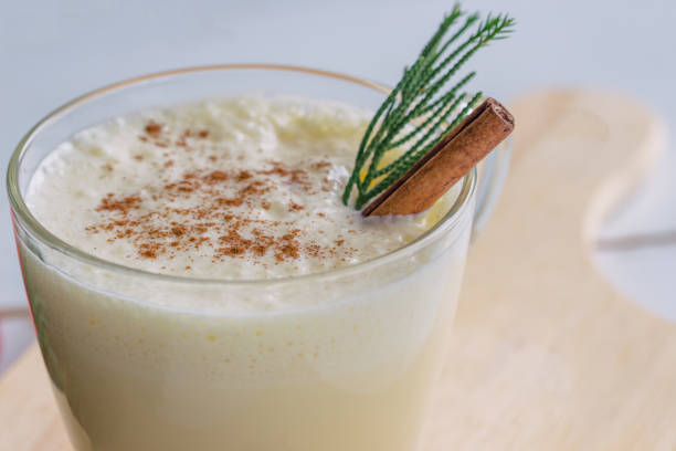 Eggnog, traditional drink for Christmas celebration party in glass topped with ground nutmeg and cinnamon stick, close up in side view. Concept to present Xmas delicious beverage.