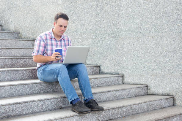 istock Busy man using laptop and drinking coffee outdoors 894337824