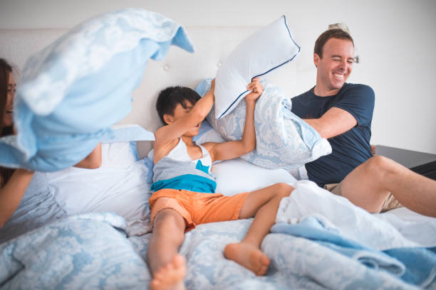 familia que tiene pillow fight en la cama - bed couple pillow fight men fotografías e imágenes de stock