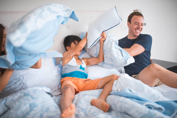 family having pillow fight in the bed - offspring child lying on back parent imagens e fotografias de stock