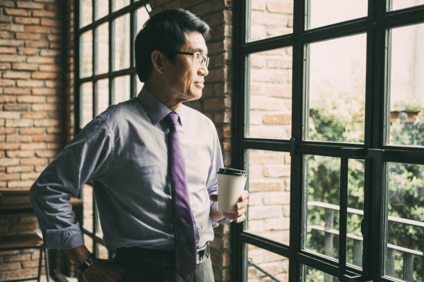 istock Thoughtful Asian Man at Window in Loft Cafe 894344678