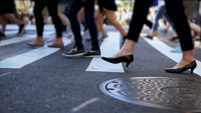 Close-up view of stylish female feet. Businesswoman crossing the road in crowded downtown. Slow motion