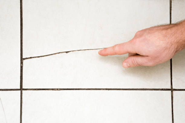 istock Man's hand finger pointing to the cracked tile on the floor. Building problems and solutions concept. 894360384