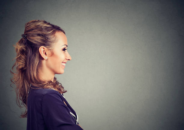 Side view of young woman posing on gray backdrop smiling cheerfully.